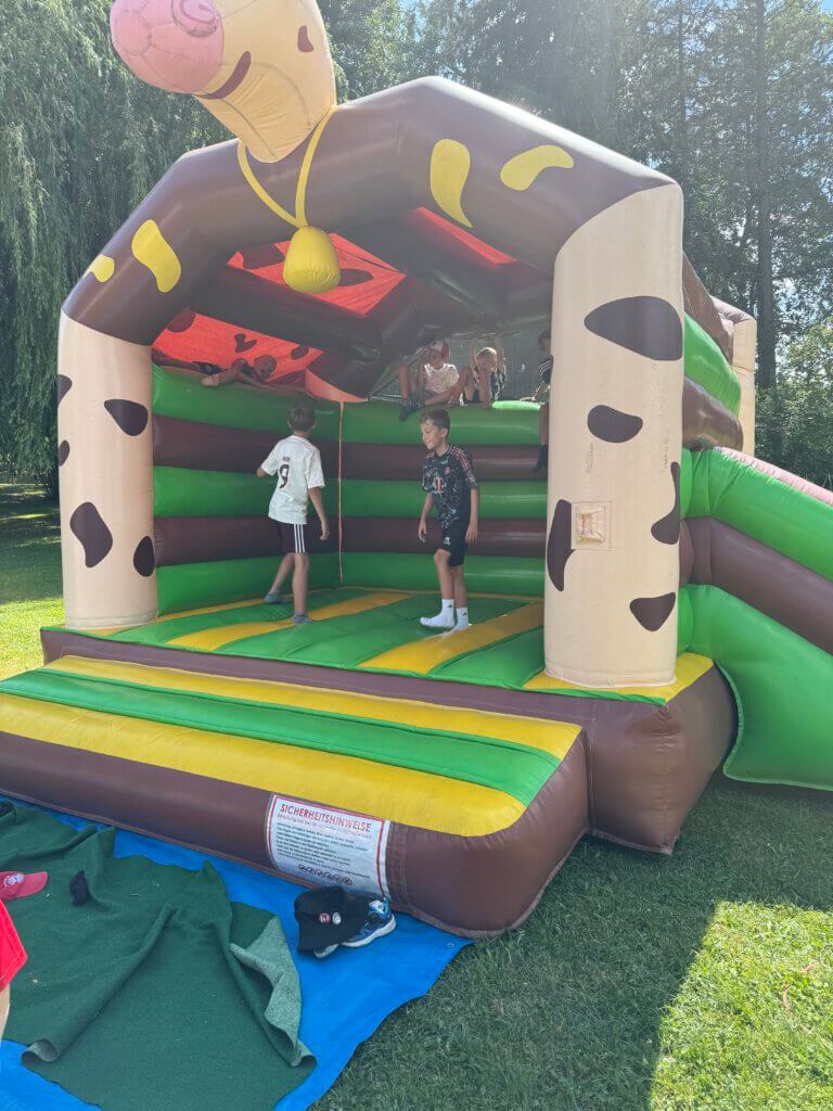 Aufgeblasene Hüpfburg im Giraffendesign mit vier darin spielenden Kindern.